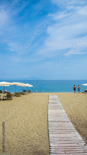 A wooden beach walkway between sun loungers and umbrellas.