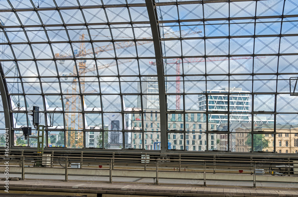 Obraz premium The end of a landscape. View of Berlin under construction - new modern buildings and cranes from within the Central Station (Berlin Hauptbahnhof). The View is overloaded with crossing lines