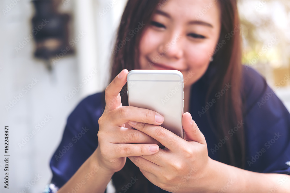 Beautiful Asian woman with smiley face using and looking at smart phone in modern cafe Beautiful Asian woman with smiley face using and looking at smart phone in modern cafe