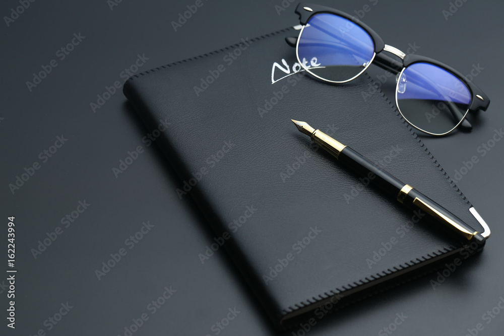 Fototapeta premium golden pen,notebook,calculator and glasses on black desk