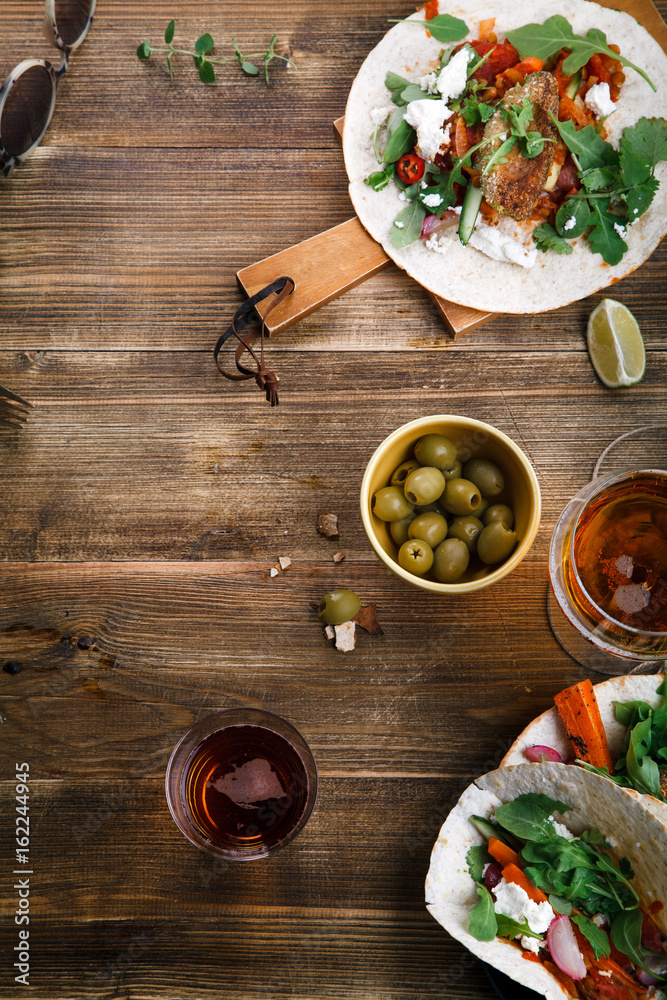 Tacos with fried avocados , tomatoes and greens on distressed wooden background. Served with beer, lime and olives. Mexican cuisine interpretation. Vertical framed composition with text space.