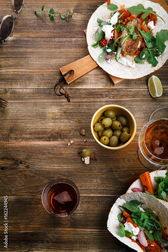 Tacos with fried avocados , tomatoes and greens on distressed wooden background. Served with beer, lime and olives. Mexican cuisine interpretation. Vertical framed composition with text space.
