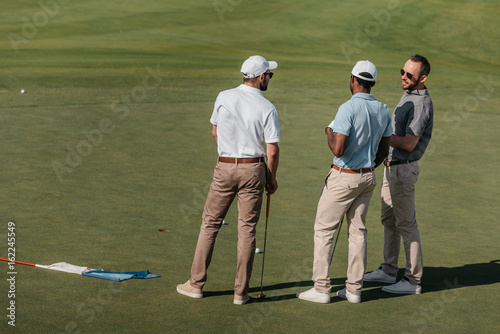 young professional golfers talking while standing on green pitch
