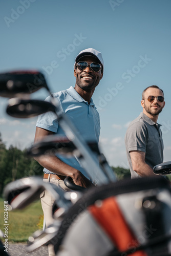 smiling multiethnic sportsmen going to the golf course, bag with clubs on foreground © LIGHTFIELD STUDIOS