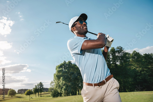 Smiling African American man in cap and sunglasses playing golf