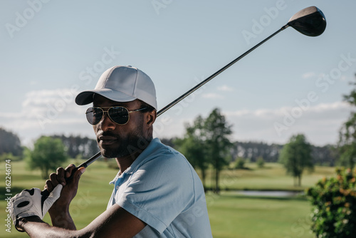 portrait of focused african american man playing golf at golf course