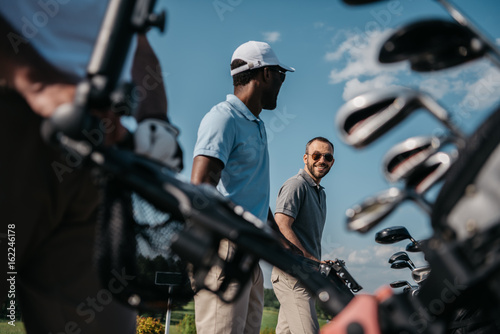 Smiling players going to the golf course, bag with clubs at foreground photo