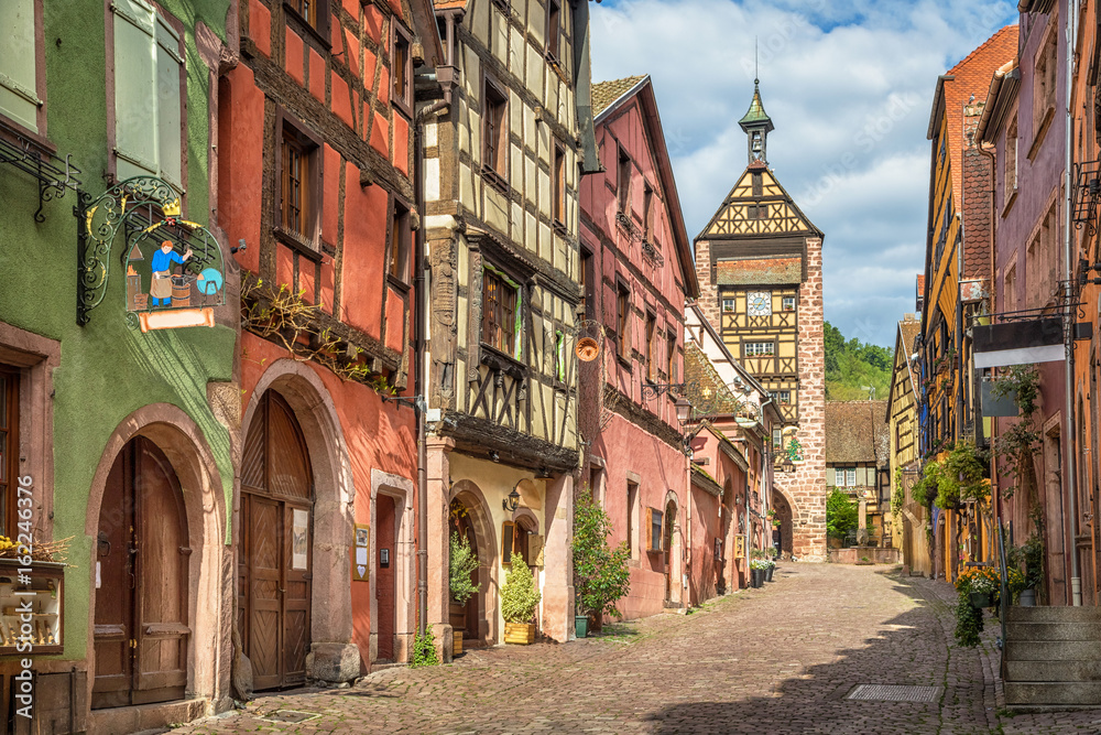 Central street of Riquewihr village with colorful traditional half-timbered french houses and Dolder Tower, Alsace, France
