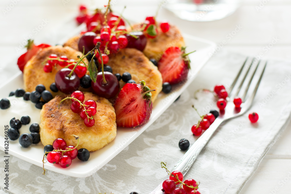 Healthy breakfast: cheese pancakes with sour cream and fresh ripe berries on white wooden table. Selective focus Healthy breakfast: cheese pancakes with sour cream and fresh ripe berries on white wooden table. Selective focus