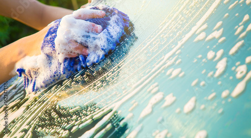 Hands hold blue sponge for washing car.