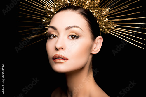 portrait of gorgeous woman in golden headpiece looking at camera isolated on black