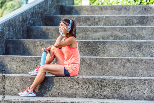 Sporty jogging girl sitting outdoors resting after training listening music