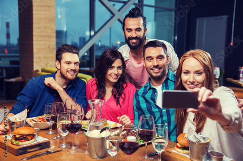 friends taking selfie by smartphone at restaurant