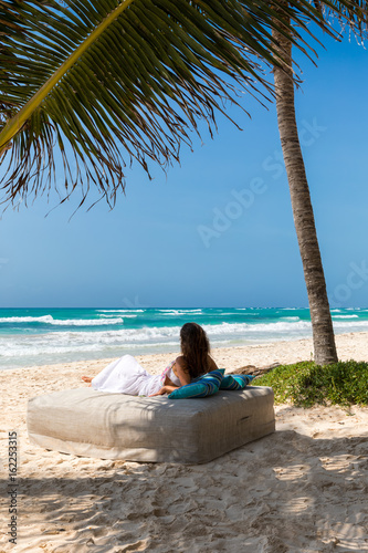 Frau liegt am tropischen Strand unter Palmen auf einer Sonnenliege und entspannt