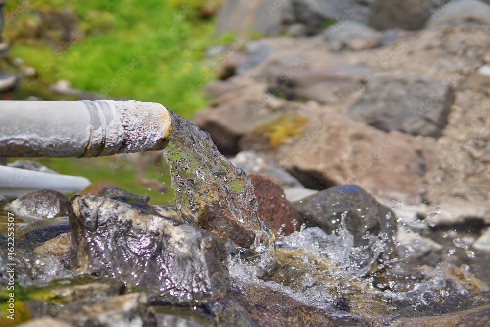 End of a rusty pipeline with a hot geothermal water flowing into the natural creek in the Icelandic natural park End of a rusty pipeline with a hot geothermal water flowing into the natural creek in the Icelandic natural park