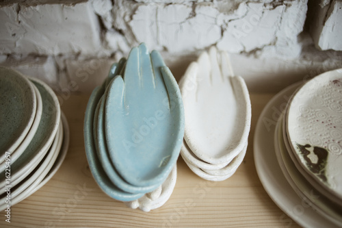 Stylish chamotte ceramic hands for rings and little things on wooden shelf with white brick wall on background in workshop