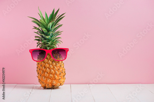 Funny pineapple in a sunglasses on table over pink background