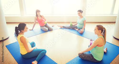 happy pregnant women sitting on mats in gym