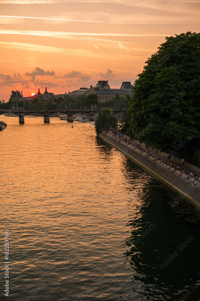 Sunset on the historic center of Paris with the river Seine and its wharves in the foreground.