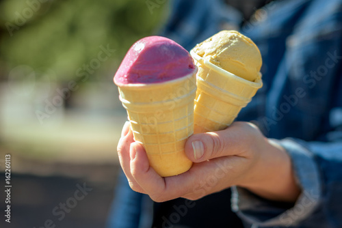 Two colorful tasty ice cream cones in hand.