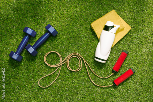 dumbbells, towel and bottle with jump rope in form of word go on the grass