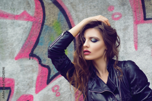 Portrait of the beautiful young woman with wavy brown hair posing outdoor, over graffiti background. Toned. © volurol