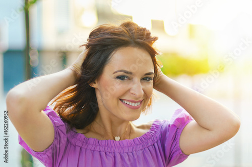 Free Download Outdoor portrait. Young beautiful woman visiting a city center during a sunny day, smiling at the camera with buildings in the background. - GFXLoad