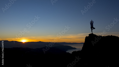 Silhouette young woman practicing yoga on top mountain at sunset