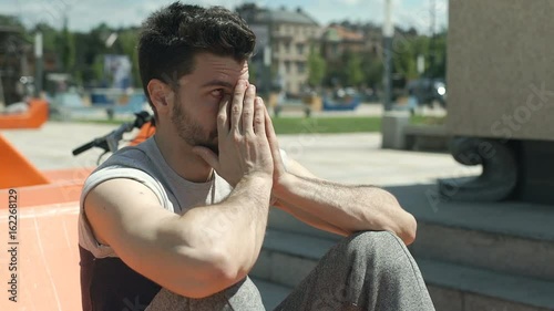 Handsome man sitting on the orange seat in the city and looks very tired, steadycam shot
