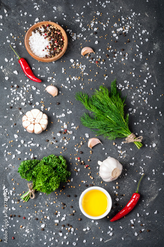 Herbs and spices on dark stone table top view. Parsley, dill, garlic, olive oil and pepper. Seasoning for cooking