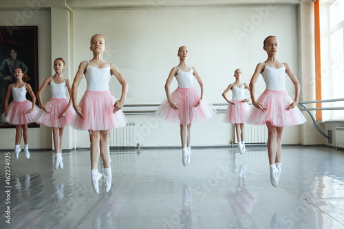 Cute little ballerinas in pink ballet costume and pointe shoes is dancing in the room. Kid in dance class. Child girl is studying ballet. Copy space.