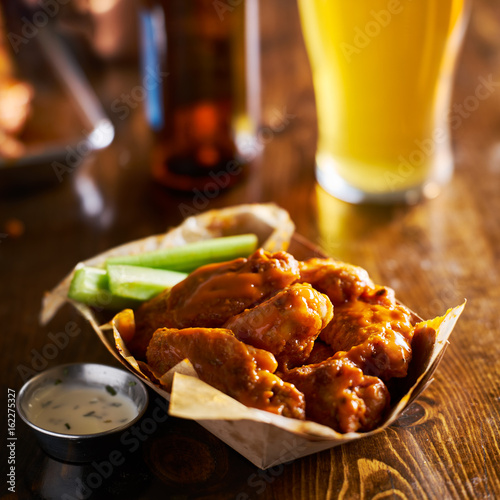 pile of tasty buffalo chicken wings in paper tray with celery and beer