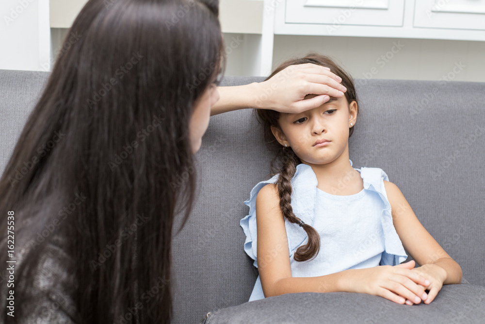Fototapeta premium Caring mother touching head on sick daughter forehead at home.