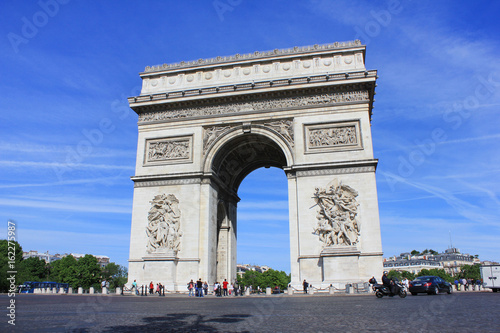 Arc de Triomphe on Champs Elysees street and Place Charles de Gaulle square in city of Paris. Famous tourist attraction landmark in Europe. Beautiful summer day scene with clear blue sky background.