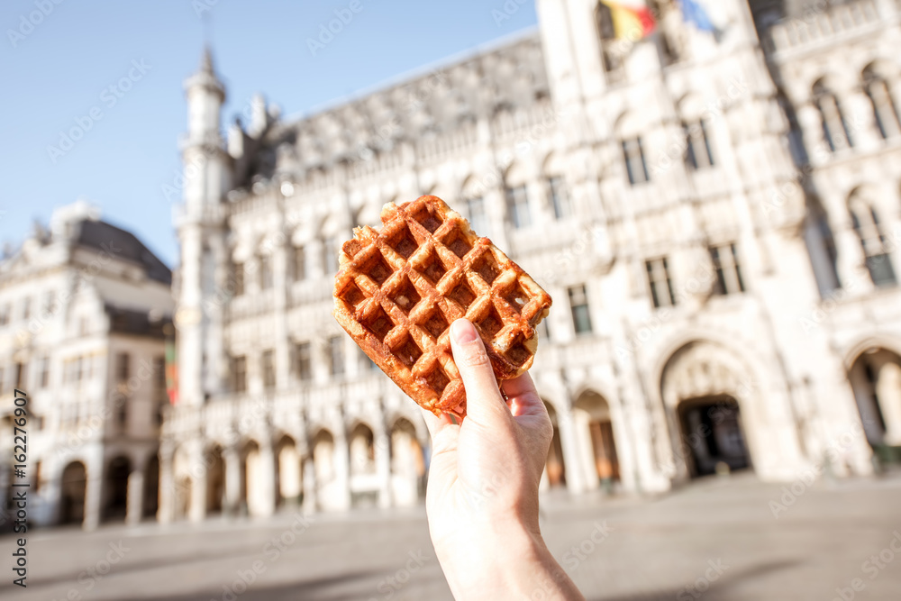 Holding a traditional belgian waffle on the central square background with city hall in Brussels. Belgian food concept