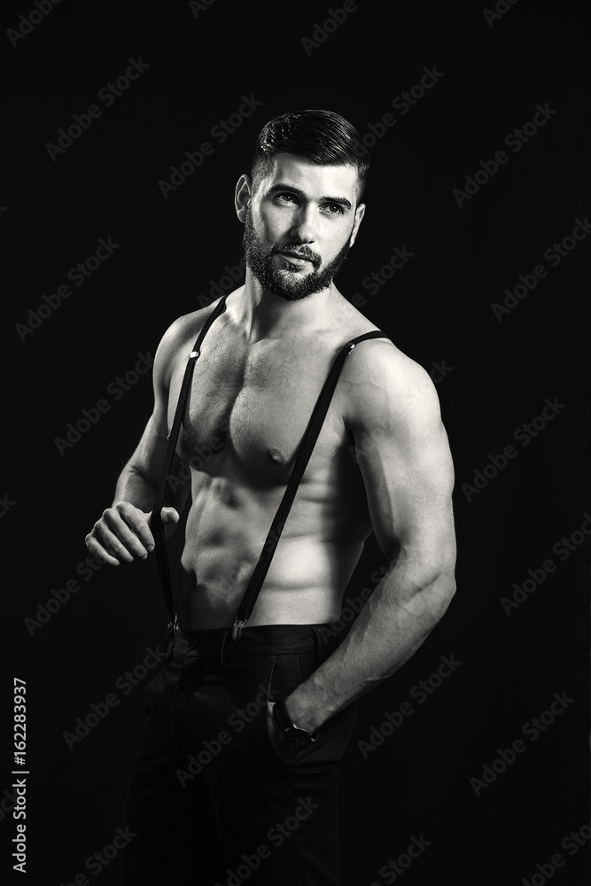 Naklejka premium Young handsome muscular man with a beard, posing on a black background