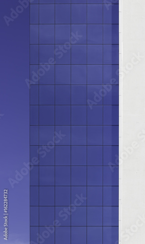 Geometric grid of windows on an office building, gradually merging with blue sky in the background. Strong vertical and horizontal lines, flat surfaces