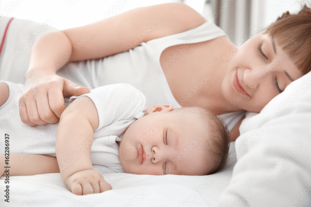 Young woman with cute sleeping baby lying on bed at home Young woman with cute sleeping baby lying on bed at home