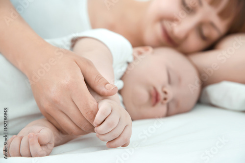 Young woman with cute sleeping baby lying on bed at home, closeup