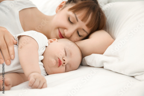 Young woman with cute sleeping baby lying on bed at home