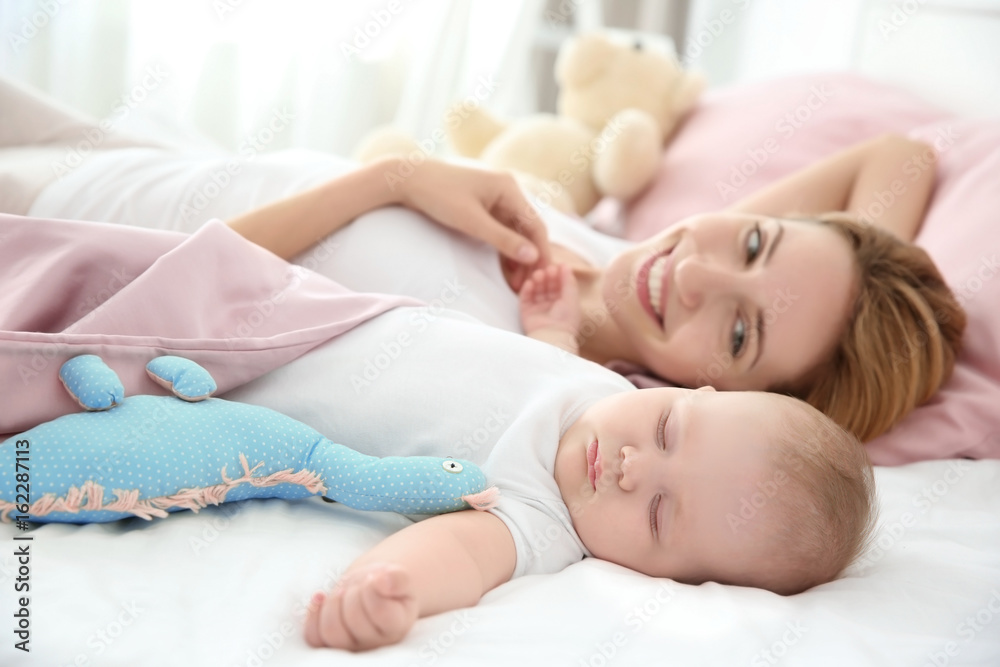 Young woman with cute sleeping baby lying on bed at home Young woman with cute sleeping baby lying on bed at home