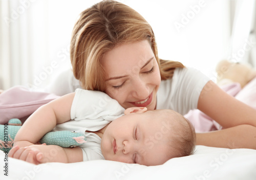 Young woman with cute sleeping baby lying on bed at home