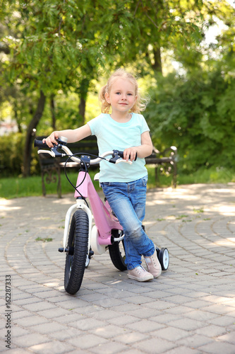 Fototapeta Naklejka Na Ścianę i Meble -  Cute girl with bicycle in park on sunny day