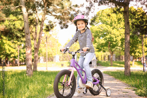 Cute girl riding bicycle in park on sunny day