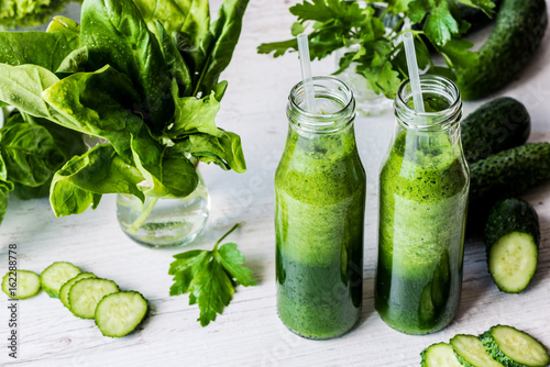 Detox diet. Two small bottles of fresh green smoothies with ingredients on a light wooden background.