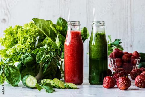Fototapeta Naklejka Na Ścianę i Meble -  Green smoothie and strawberry smoothie in two small bottles with ingredients on a light wooden background. Healthy detox drinks.