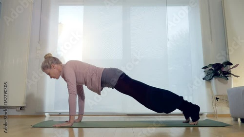 A woman transitions from the downward dog yoga position to the one legged dog position. photo