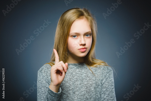 displeased and contemptuous girl with threatens finger on gray background