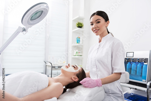 Charming beautician is laboring with female face