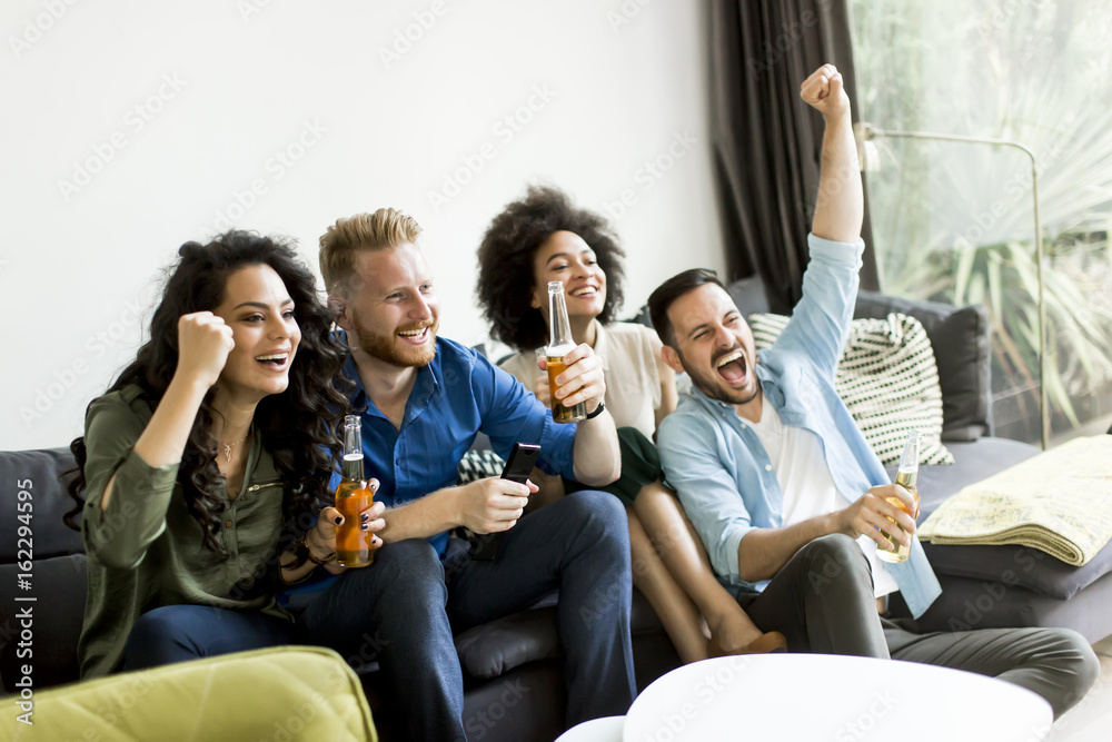 Friends watching TV , drinking cider and having fun in the room